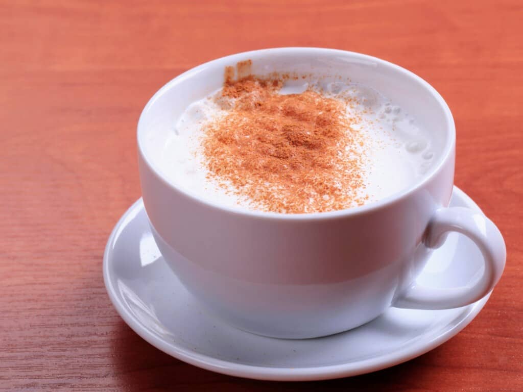 babyccino served in a white cup with a dusting of cinnamon on a wooden background