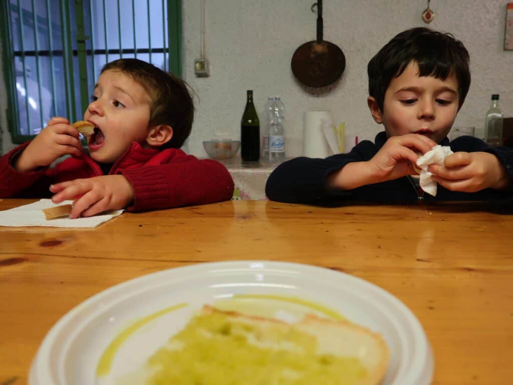 two boys eating fettunta in foreground wooden tale with white plate with fettunta