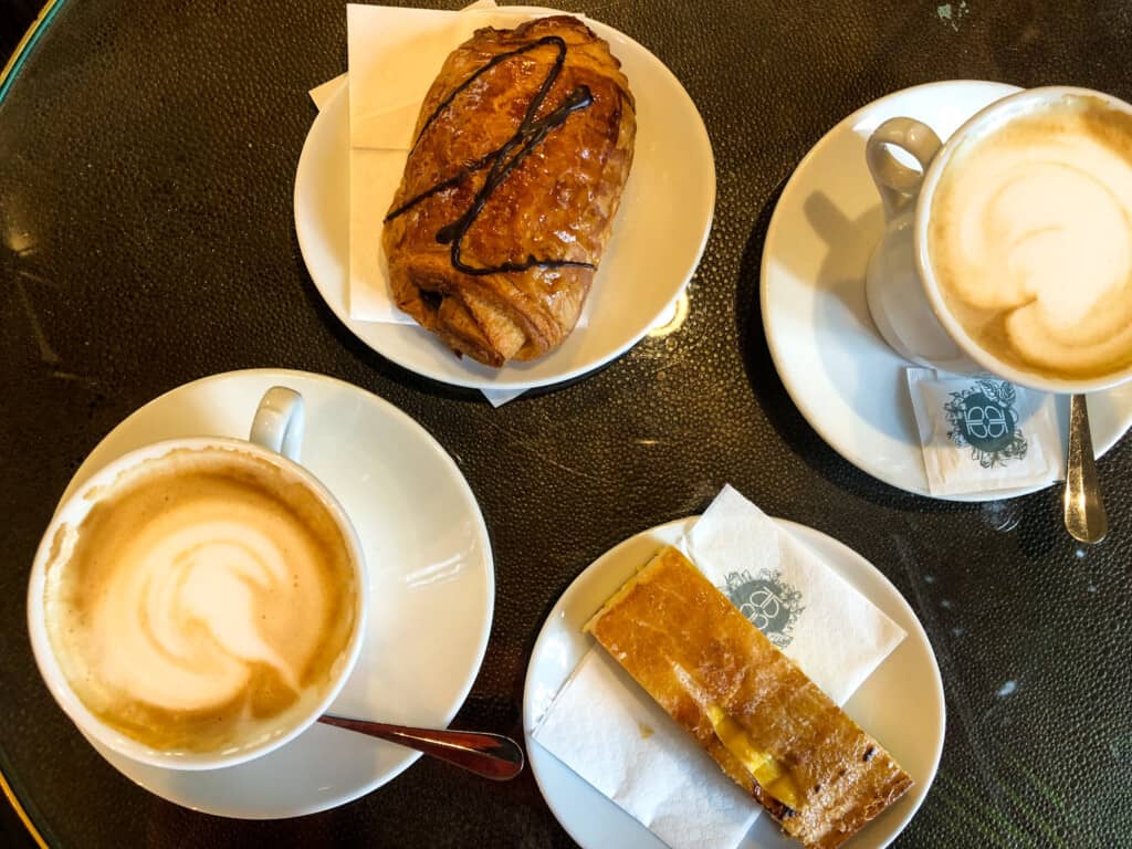 top view of two cappuccino and two pastries on white plates on a wooden table