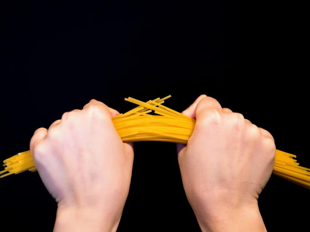 two hands breaking spaghetti on a black background close up - horizontal image