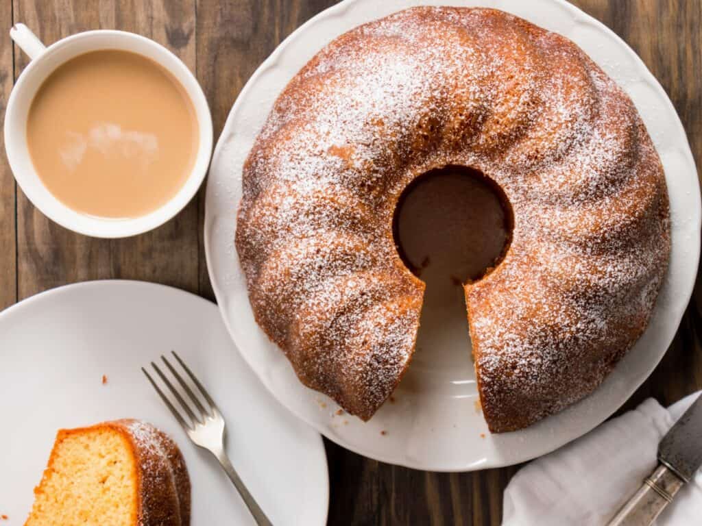 Slice of bundt cake served with a cup of coffee with milk and whole cake next to it. birds eye view. 