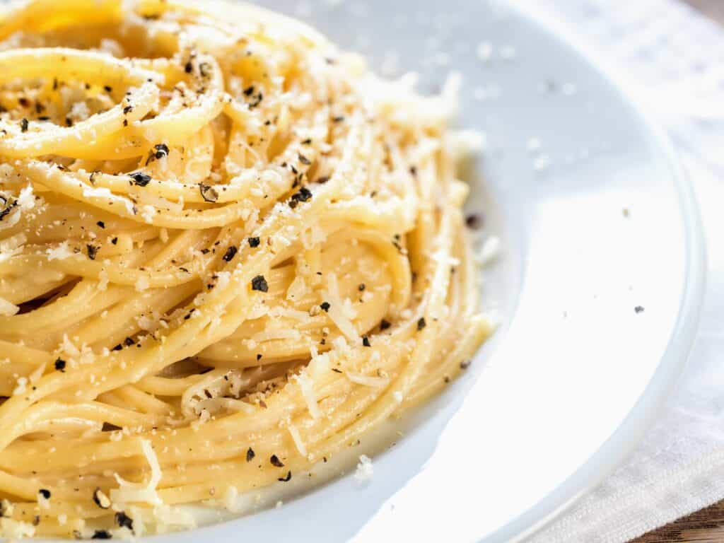 white plate with close up of spaghetti in cheese and black pepper corns