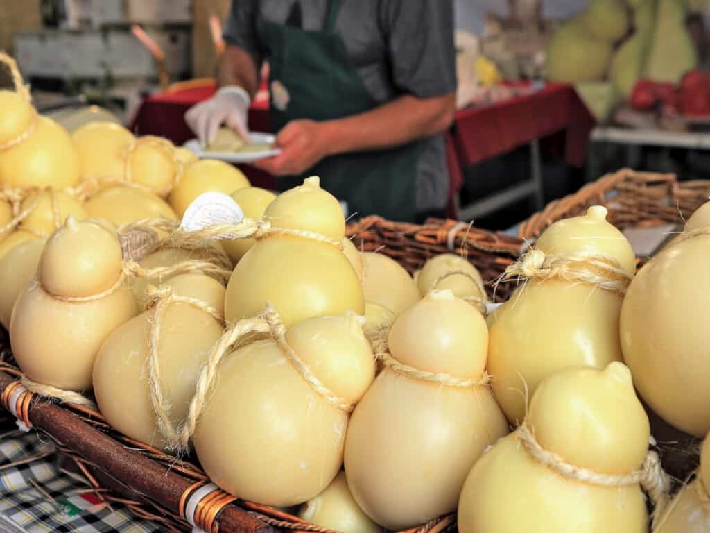 caciocavallo lined up on a table at an outdoor market ready to be sold with a man in the background
