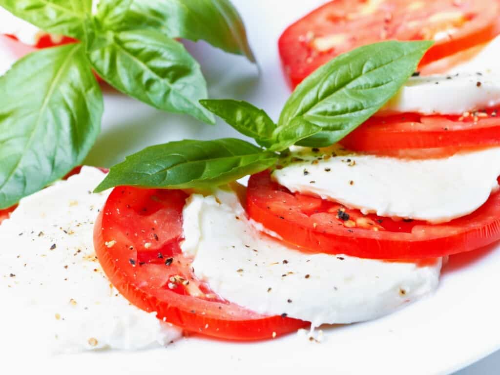 close up of sliced mozzarella and seasonal red tomatoes garnished with basil and black pepper