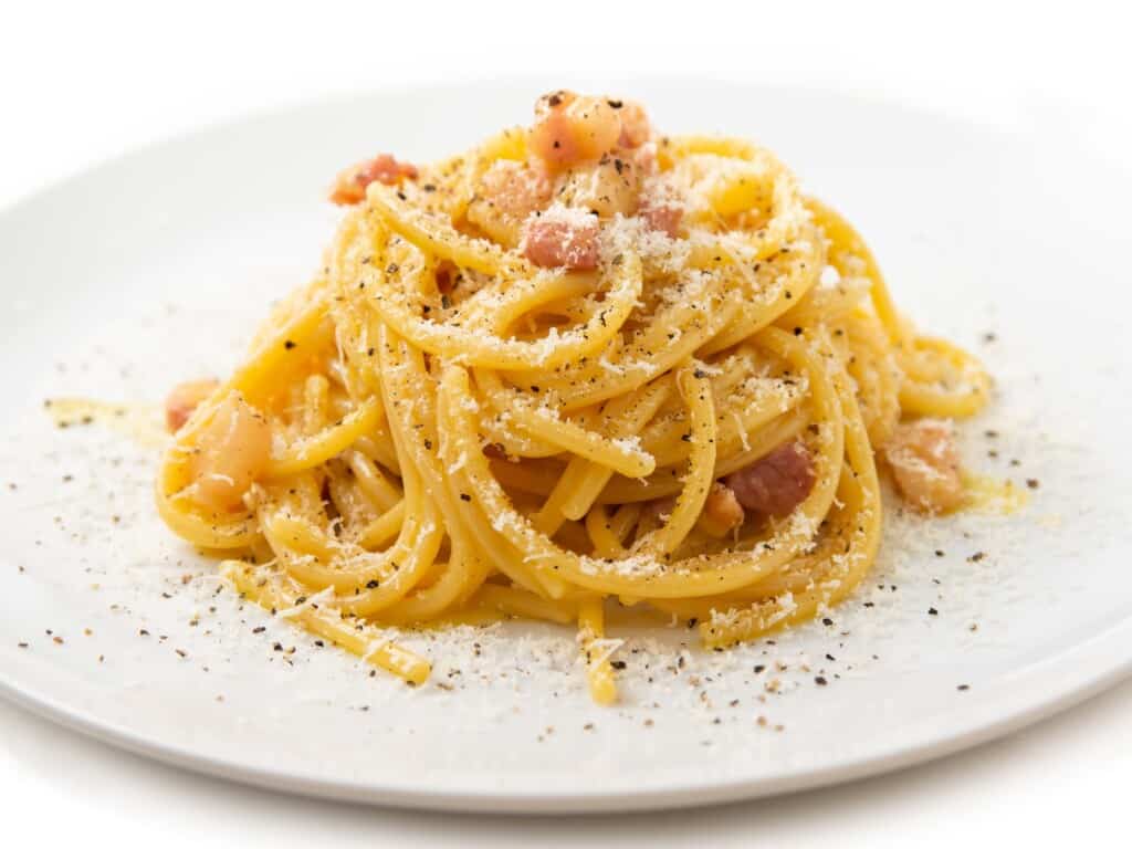 italian carbonara served on a white plate garnished with pancetta and black pepper