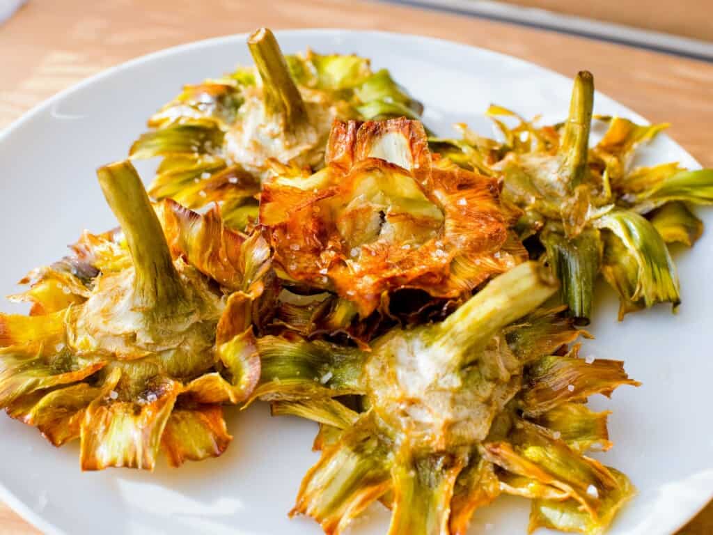 various fried artichokes served on a white platter on a wooden table