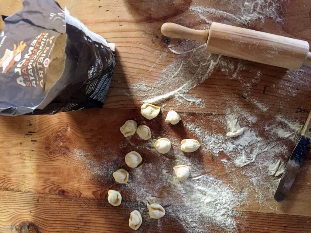 top view of cutting board with homemade orecchiette pasta, a rolling pin and a bag of flour on a wooden board