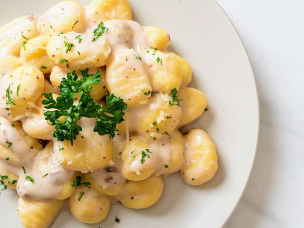 gnocchi alla bava served on a white plate in cream sauce garnished with parsley on marble background