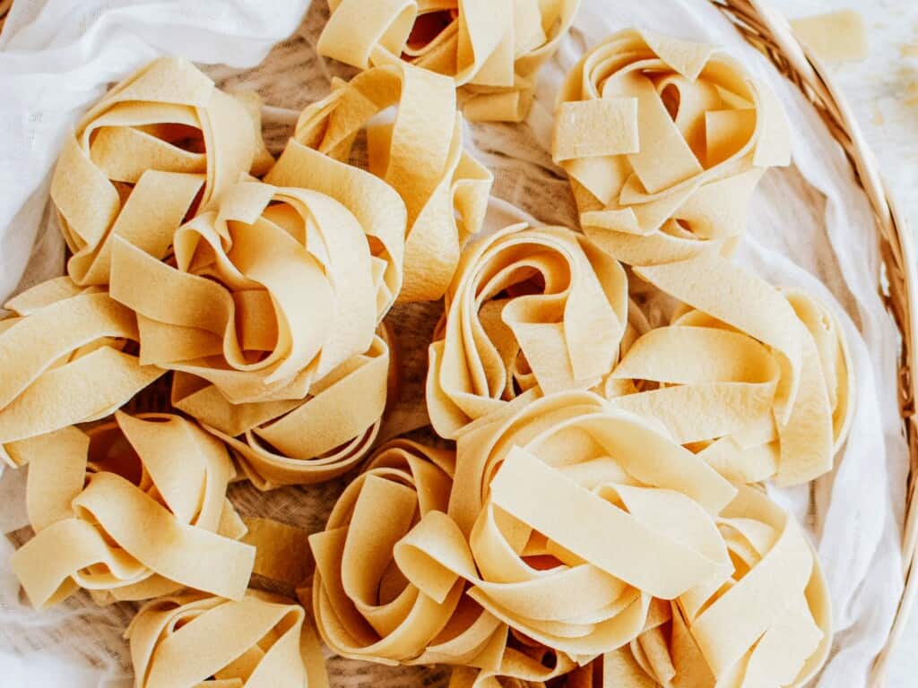nests of homemade pappardelle uncooked on a white background