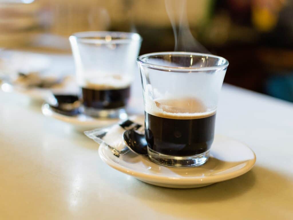 side view of two glass espresso cups with espresso on white plates on a white counter