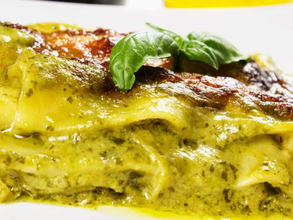 lasagne with potatoes and pesto close up on white platter garnished with basil