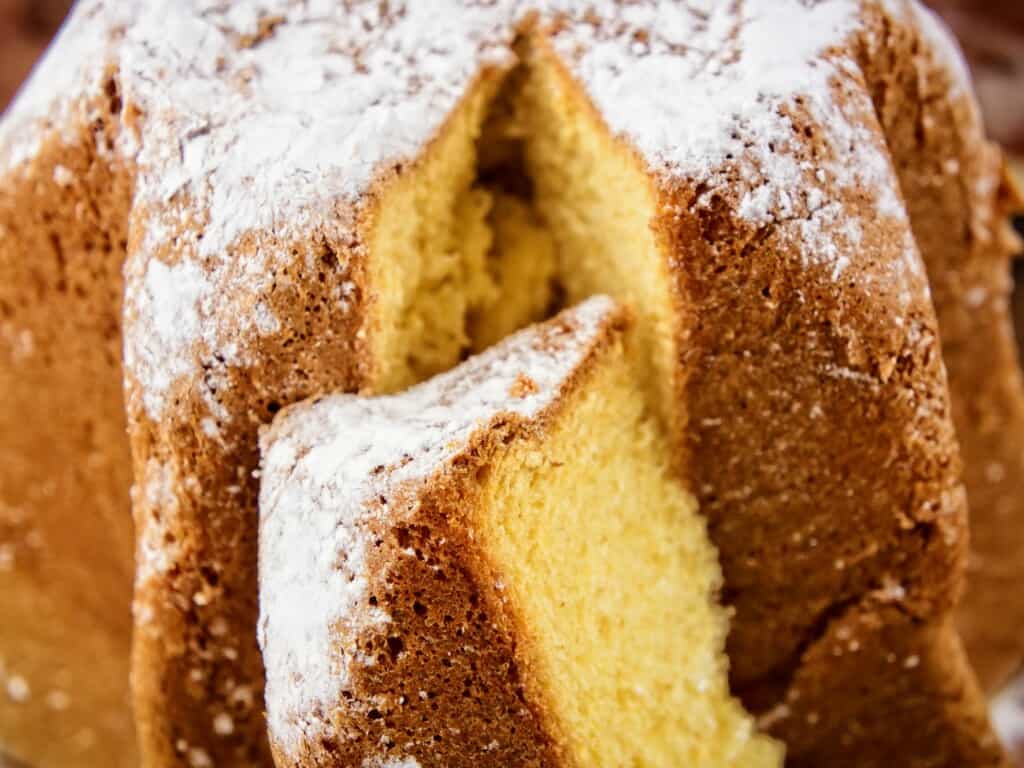 zoomed in on pandoro with a slice cut out dusted in powdered sugar
