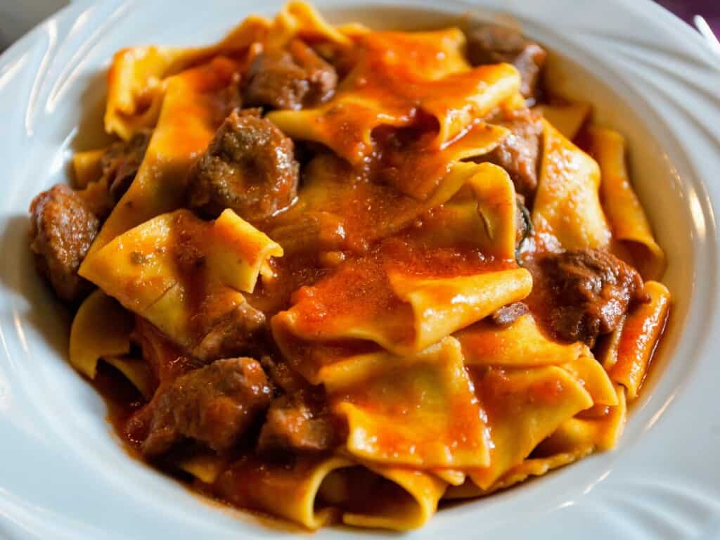 shallow white bowl filled with pappardelle pasta coated in wild boar sauce