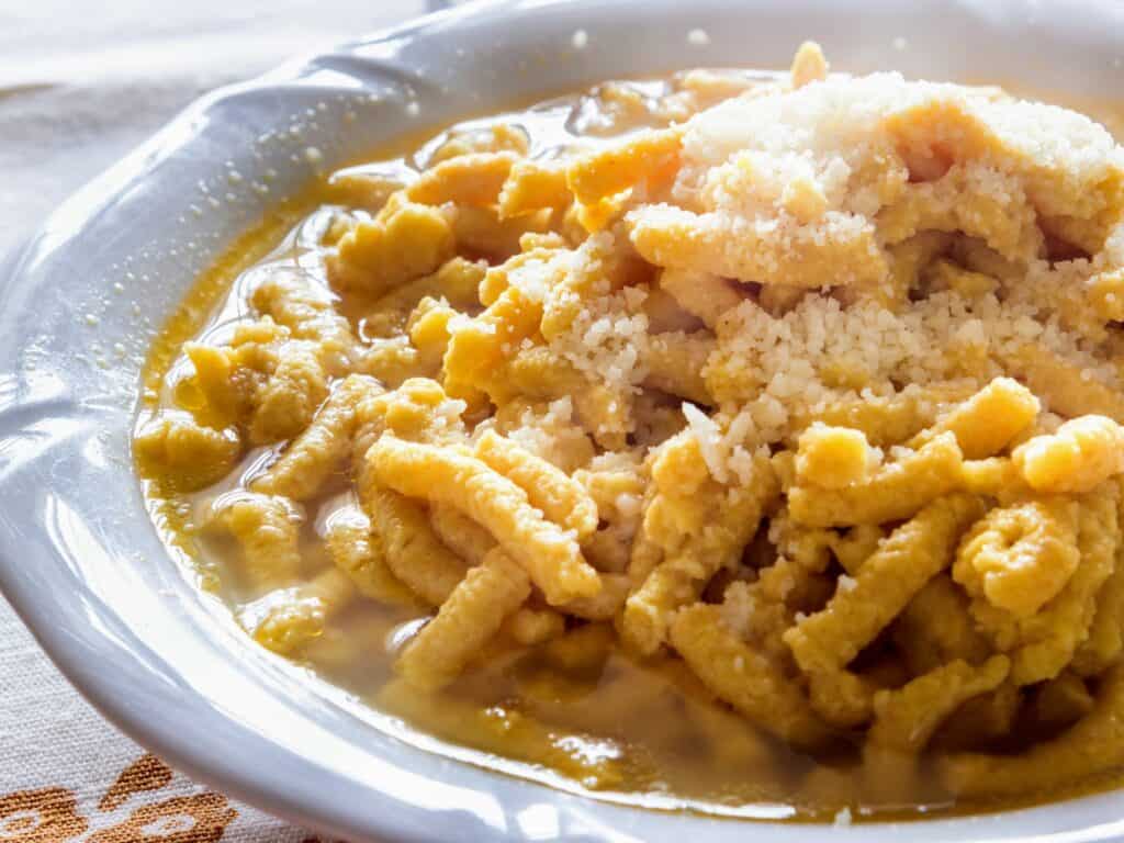 a shallow white bowl filled with passatelli in broth topped with grated parmesan cheese