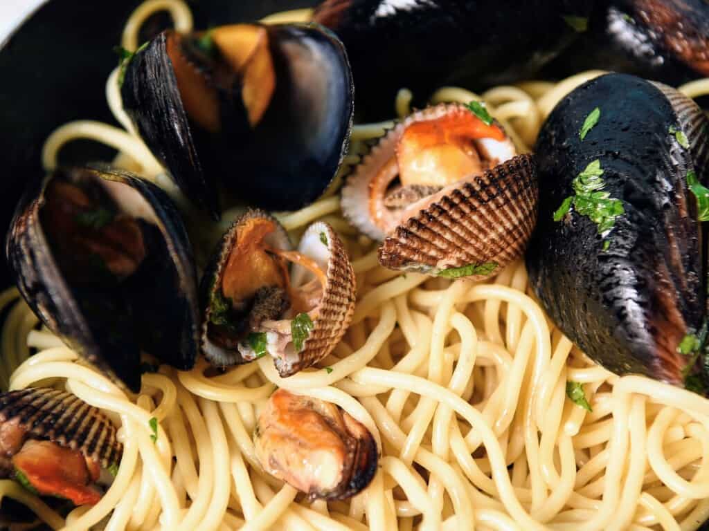 close up of spaghetti cooked with various seafood such as clams and mussels garnished with parsley