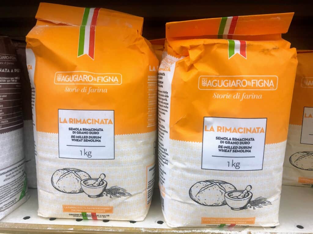 orange and white bags of semola flour on grocery store shelf zoomed in.