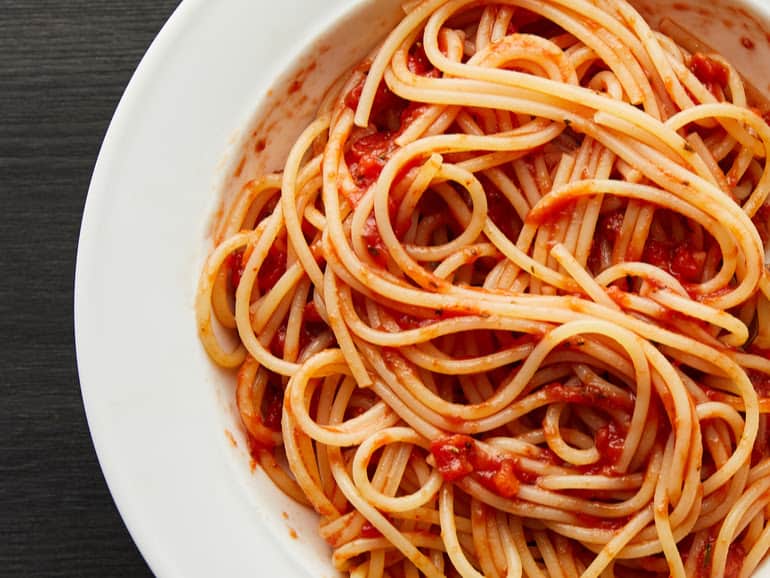 close up of white shallow bowl with spaghetti in tomato sauce on black background