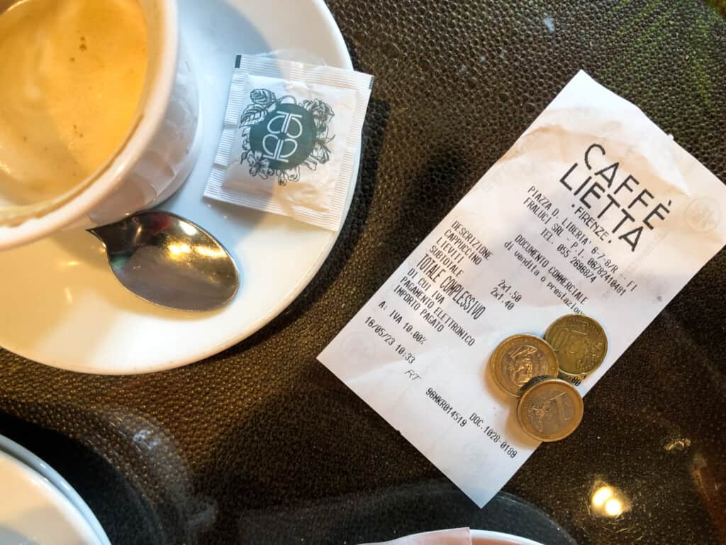 top view of a receipt with coins left for a tip on a wooden table with a corner of a cup and saucer on the left hand corner