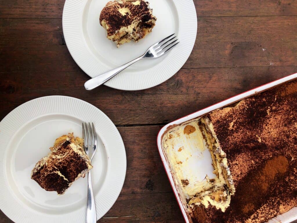 Tiramisu in a dish and on plates on a wooden table.