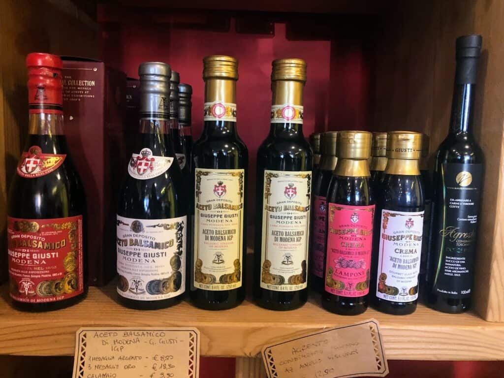side view of several balsamic vinegars on a shelf for sale with small handwritten signs underneath with price