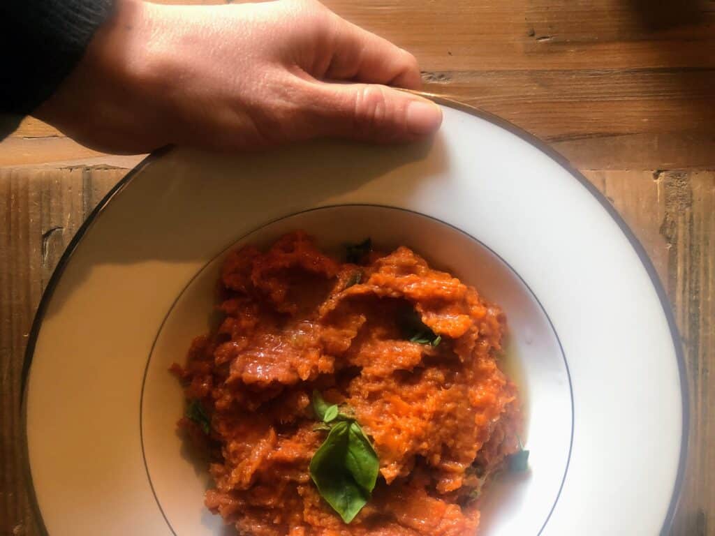 Hand holding white bowl of pappa al pomodoro over a wooden table.
