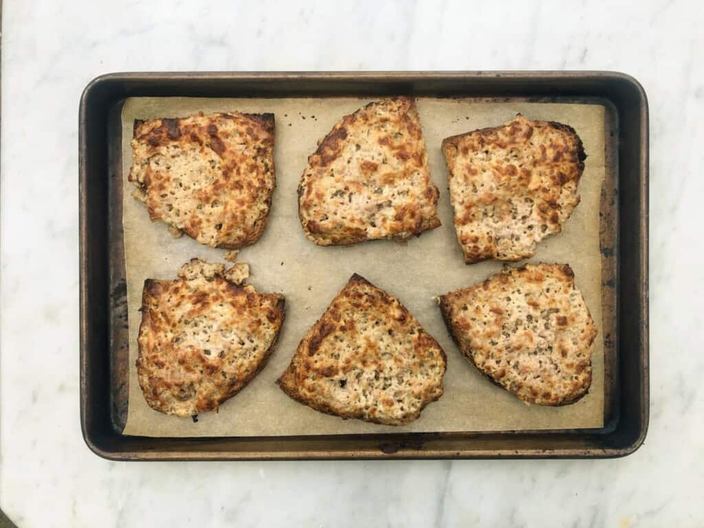 top view of marble board with baking sheet with sausage and bread crostini