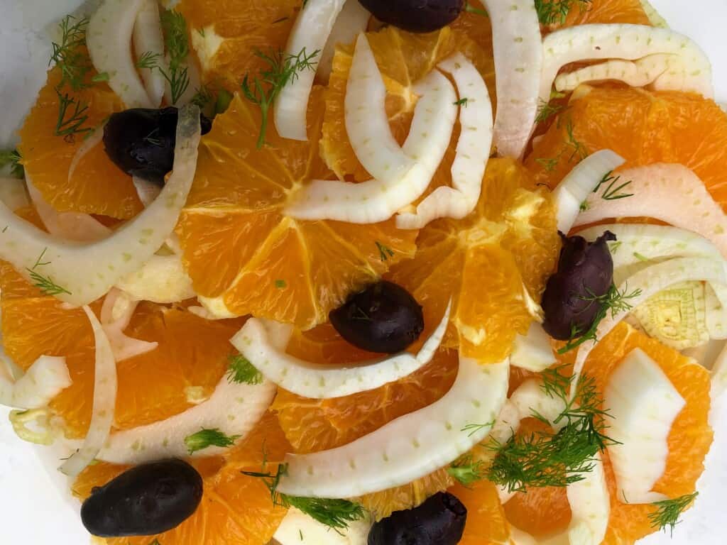 close up top view of fennel and orange slices on a plate garnished with olives and fennel tops.