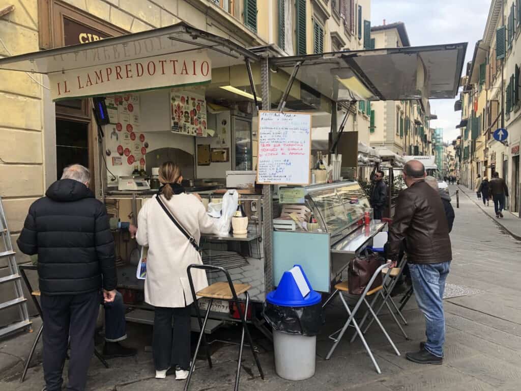 view of food stall from street in florence with lots of people gathered around eating sandwiches.