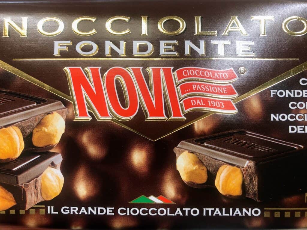 Close up of wrapper of Novi chocolate bar.  Brown wrapper with red text and photos of the chocolate bar with hazelnuts inside.