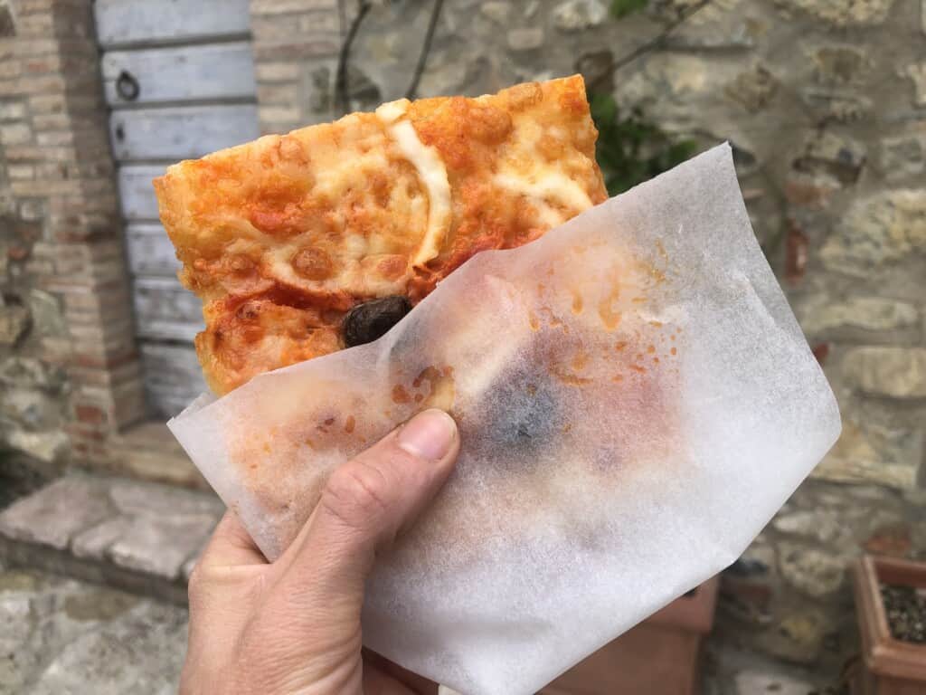 hand holding a piece of pizza wrapped in parchment paper