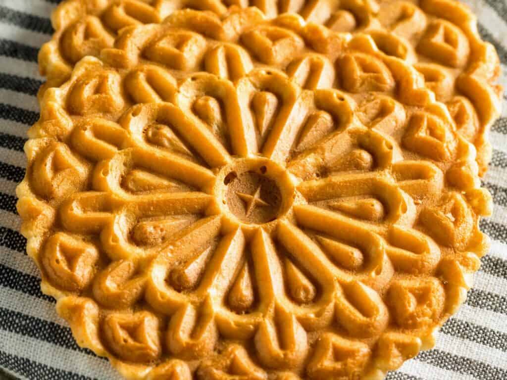 Close up of pizzelle, a type of pressed Italian cookie, sitting on a black and white striped tea towel.