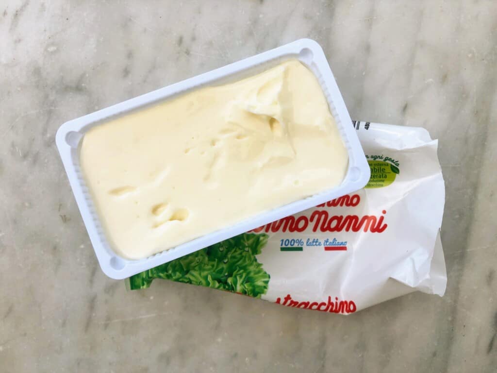 top view of marble countertop with a package of open stracchino cheese in white plastic container