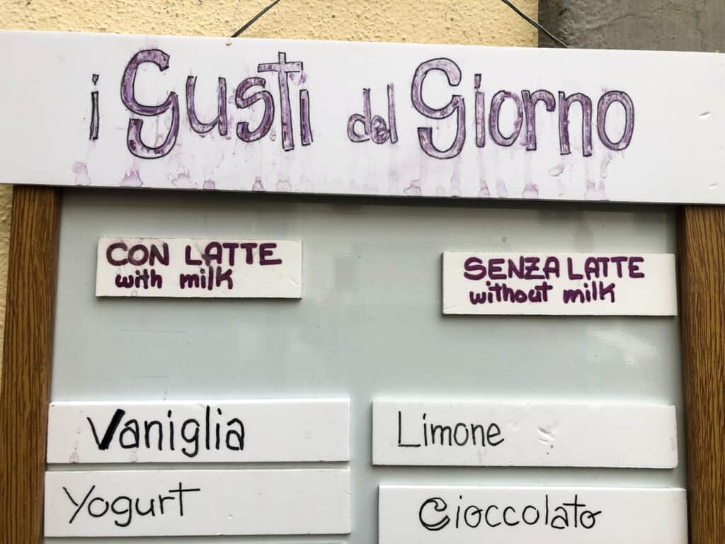 Handwritten sign listing gelato flavors with and without milk at a gelateria in Italy.