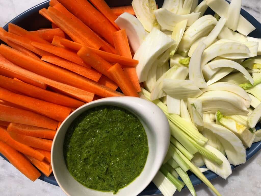 Close up of a platter of sliced carrots, celery, and fennel with a small bowl of Tuscan green sauce.