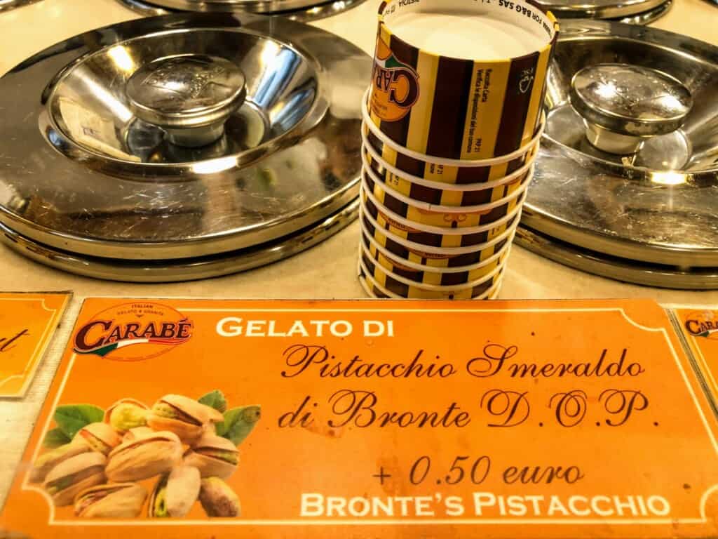 Sign for pistacchio flavored gelateria in a gelateria in Italy. You can also see gelato cups and metal containers of gelato behind it.