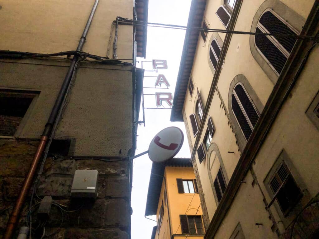 image of italian streets from below with BAR sign and round circle sign with phone booth symbol