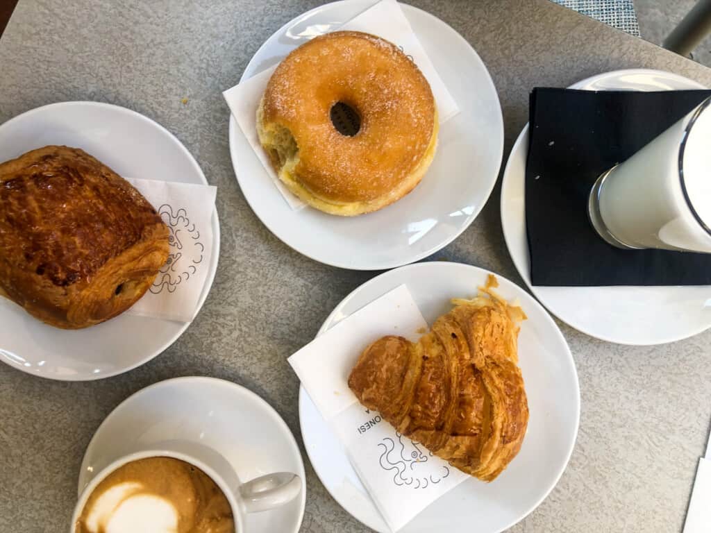 close up top view of breakfast pastries on white plates with various coffee beverages on a white table 