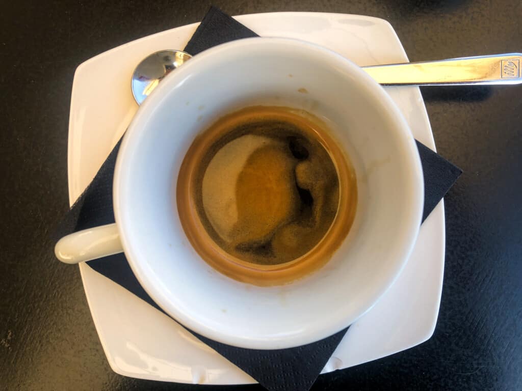 top view of white espresso cup on a white saucer with a black napkin and a spoon on the side on a black countertop