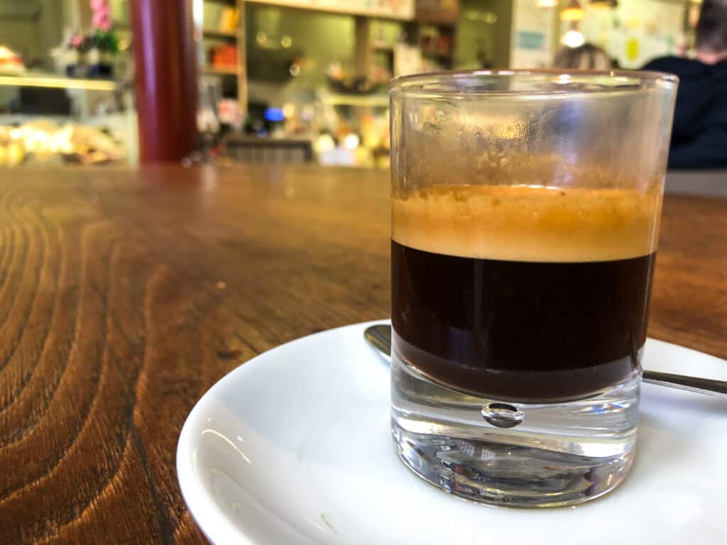 side view of a caffe in vetro in a small white glass on a white saucer on a wooden table