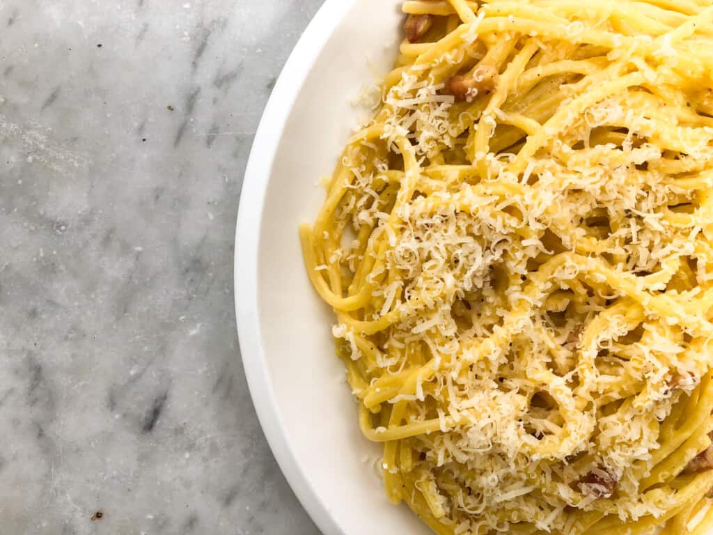 top view close up of a white plate with carbonara spaghetti topped with cheese on a marble background