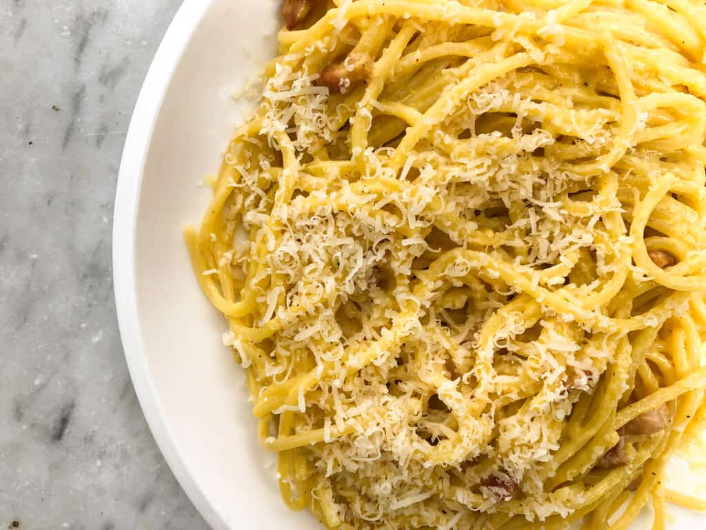 top view close up of a white plate with carbonara spaghetti topped with cheese on a marble background