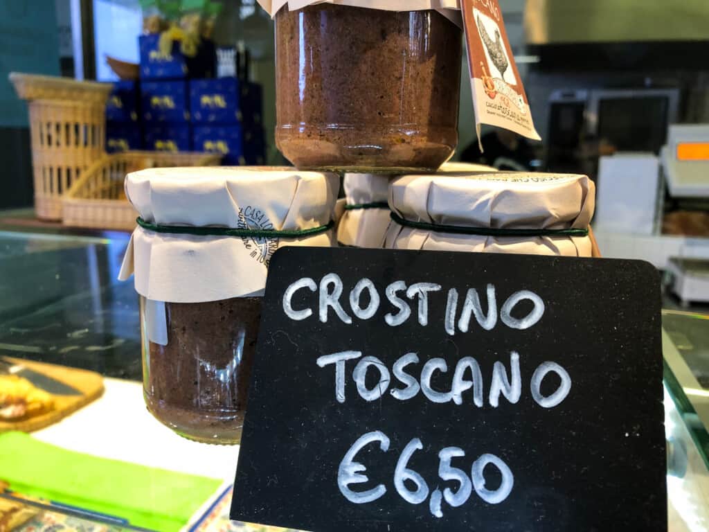 side view of a small black sign reading crostino toscano with price with jars of liver pate.