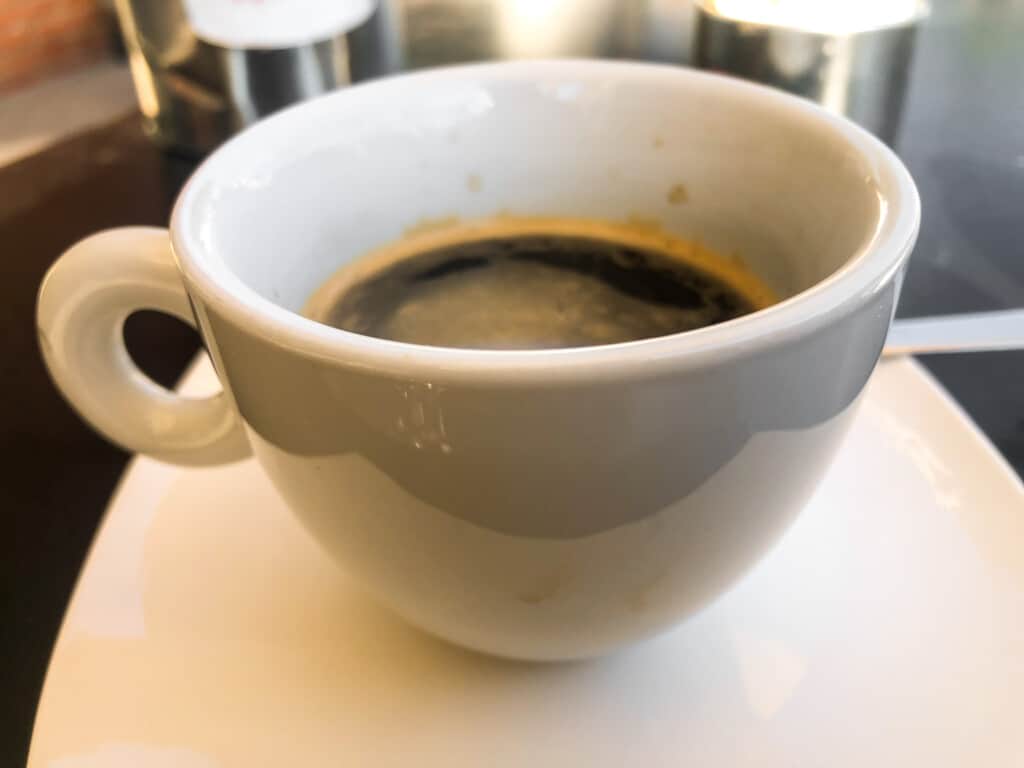side view of a white espresso cup filled with a double espresso with black in the background