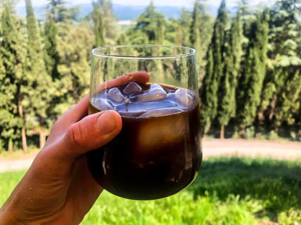 hand holding a glass of cafe freddo outdoors with a backdrop of the tuscan countryside