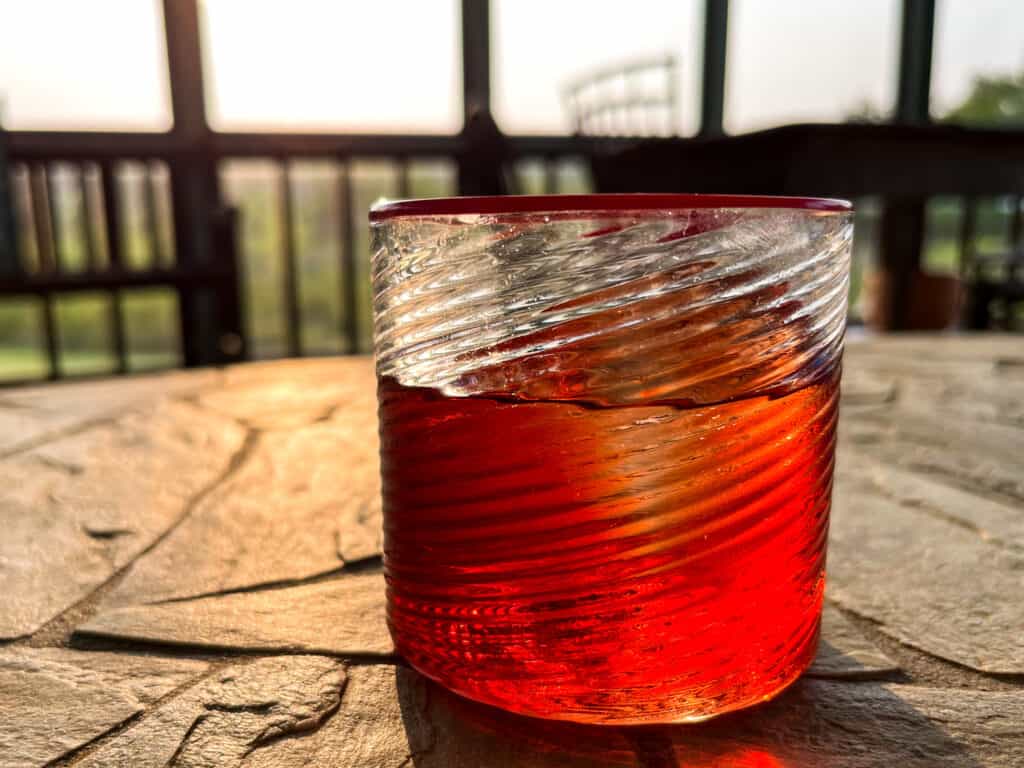 close up of tumbler glass with red rim on a stone table filled with ice and a bright red negroni