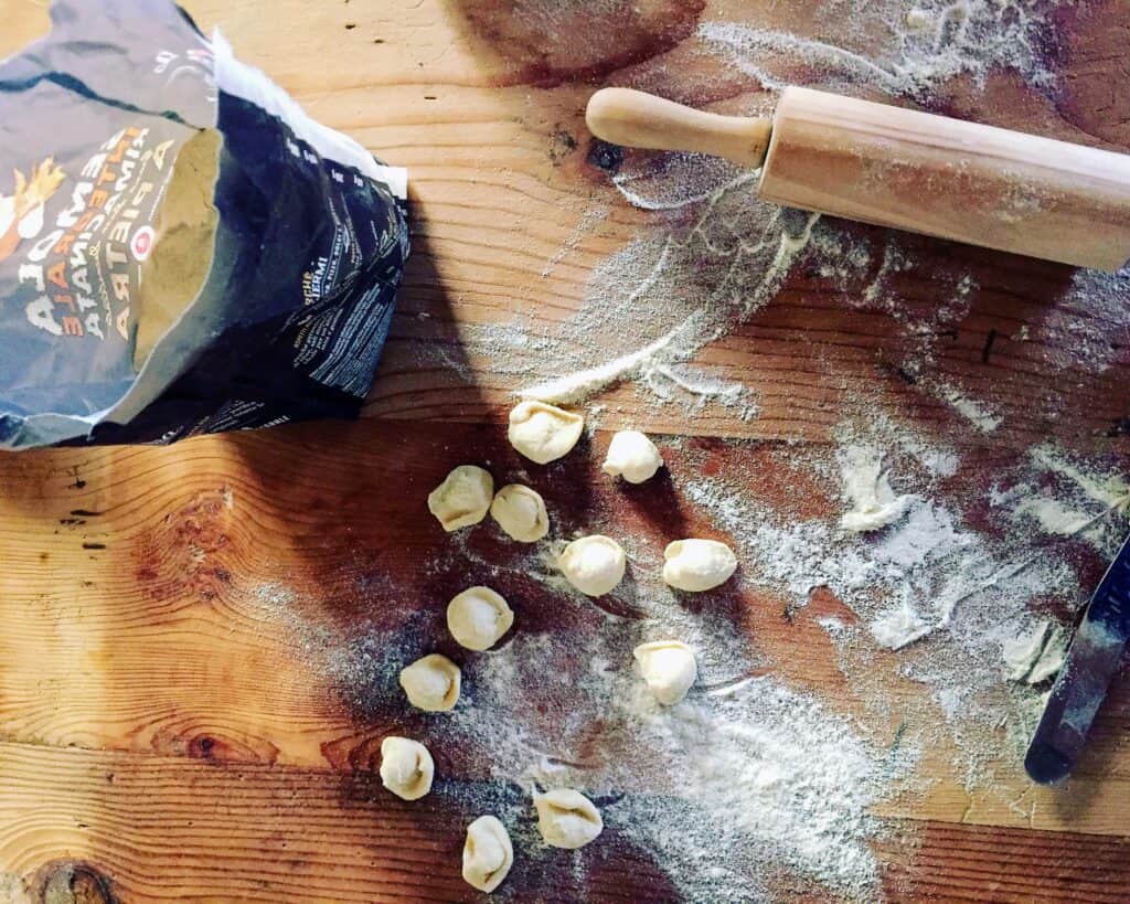 top view of wooden board with homemade pasta scattered with a sack of flour and rolling pin.