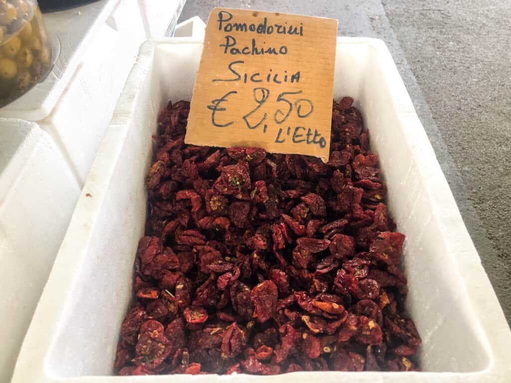 close up of white box with pomodorini /sun dried tomatoes secchi for sale with a cardboard sign indicating price