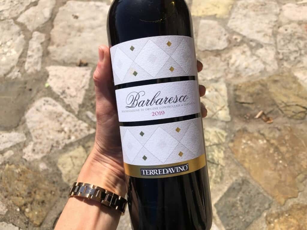 Hand holding a bottle of Barbaresco over a stone surface.