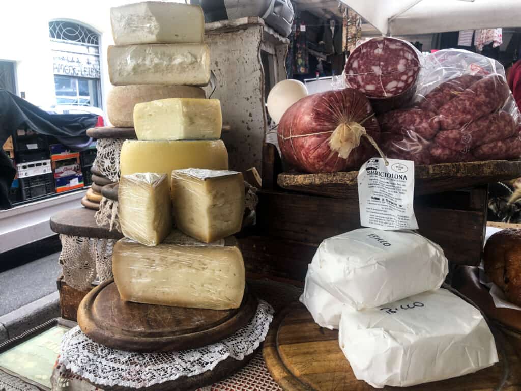 various cheeses, including pecorino stacked on a wooden table with salami for sale at a market. some are cut open, others are full, round forms