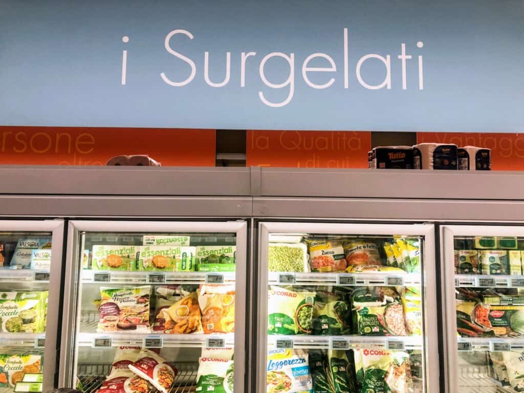 View of frozen area of a grocery store in Italy. You can see packaged vegetables in the glass display cases.